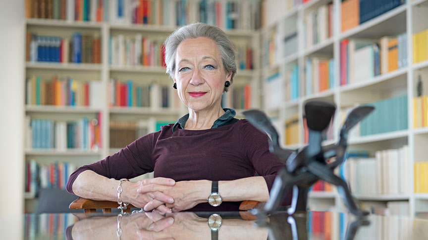 Professsor Dr Gesine Lenore Schiewer sitting at a table, a bookshelf behind her.